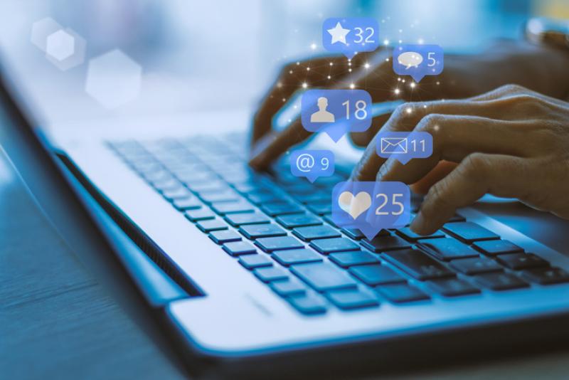 Someone typing on laptop with social media symbols